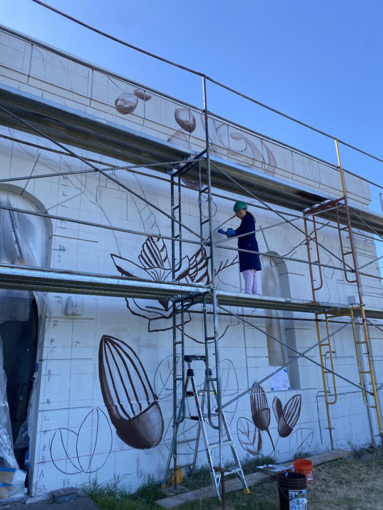 qi han artist on the scarfolding painting a mural featuring a giant oal.